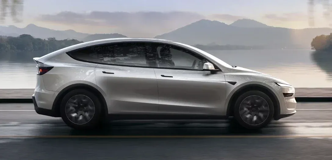 خودروی برقی Tesla Model Y نقرهای در حال رانندگی کنار دریاچه